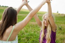 Young women with arms raised and hands held — Stock Photo