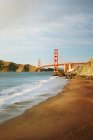 Scenic view of Golden Gate Bridge at dusk with a person and their dog on Marshall's Beach in the foreground. San Francisco, California, USA — Stock Photo
