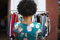 Rear view of young female fashion blogger with afro hair looking at vintage clothes rail, New York, USA — Stock Photo