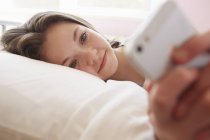 Chica acostada en la cama mensajes de texto en el teléfono inteligente - foto de stock