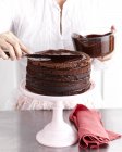Imagen recortada de la mujer glaseado pastel capa de chocolate - foto de stock