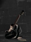 Smashed acoustic guitar beside black wall — Stock Photo