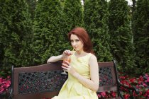 Молода жінка п'є сік на лавці парку — стокове фото