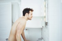 Jovem olhando no espelho do banheiro — Fotografia de Stock