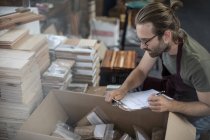 Uomo con appunti che controlla i prodotti in scatola in fabbrica — Foto stock
