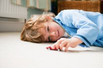 Jeune garçon couché sur le côté jouant avec une voiture jouet — Photo de stock