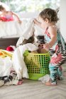 Female toddler removing laundry from child hiding in laundry basket — Stock Photo