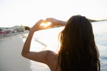 Mulher fazendo forma de coração em torno do sol — Fotografia de Stock