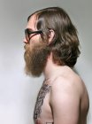 Jovem com barba e tatuagens no peito, vista lateral — Fotografia de Stock