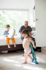 Brother drumming on bed, sister playing superhero while father watch on — Stock Photo