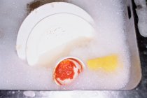 Dishes soaking in soapy water with foam — Stock Photo