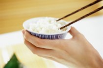 Female hand holding bowl of rice and chopsticks — Stock Photo