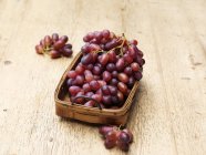 Red grapes in vintage wicker basket on wood — Stock Photo