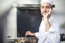 Retrato del chef agitando la cacerola en la estufa, señalando con los dedos a los labios - foto de stock
