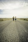 Rear view of young  couple running hand in hand on road, Cody, Wyoming, USA — Stock Photo