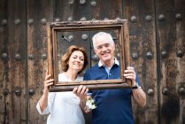 Portrait of senior couple, holding wooden frame in front of their faces, Mexico City, Mexico — Stock Photo