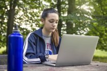 Teenage girl in park using laptop at picnic bench — Stock Photo