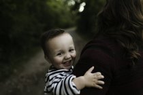 Bébé garçon dans les bras de la mère regardant la caméra sourire — Photo de stock