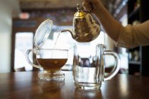 Mão feminina derramando chá no balcão do café — Fotografia de Stock