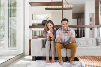 Casal jogando jogos em smartphones no sofá da sala de estar — Fotografia de Stock