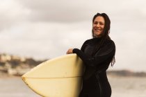 Молодая женщина уходит из моря, неся доску для серфинга — стоковое фото