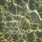 Rayos de sol que rompen el agua de mar en el fondo arenoso - foto de stock