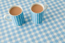 Vue rapprochée de deux tasses de thé avec du lait sur fond motif damier — Photo de stock