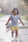 Chica descalza corriendo a través de charcos en la calle lluviosa - foto de stock