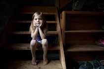 Little girl sitting on basement steps, looking at camera — Stock Photo