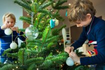 Niños decorando el árbol de Navidad con bolas en casa - foto de stock