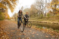 Счастливая молодая пара катается на велосипеде вдоль берега реки осенью — стоковое фото