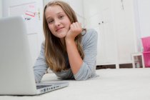Smiling girl using laptop on floor, focus on foreground — Stock Photo