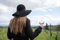 Женщина, стоящая в винограднике, держащая бокал вина, вид сзади — стоковое фото