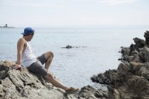 Visão lateral completa do jovem sentado sobre rochas olhando para o oceano, Stintino, Sardenha, Itália — Fotografia de Stock
