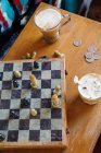 Tablero de ajedrez con bebidas y monedas en la mesa - foto de stock