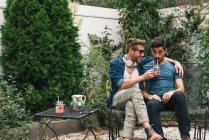 Jovem casal masculino sentado no jardim bebendo coquetéis — Fotografia de Stock