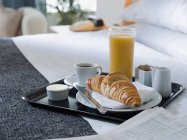 Frühstückstablett mit Kaffee, Croissant und Saft auf dem Bett — Stockfoto