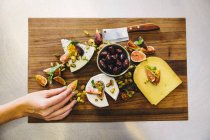 Variety cheese plate with figs, olives, pistachios, cleaver on wooden chopping board — Stock Photo