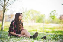 Молодая женщина сидит на траве в парке и слушает наушники — стоковое фото