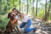 Retrato de adolescente abraçando cão bonito no caminho da floresta — Fotografia de Stock