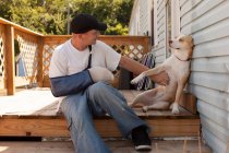 Man outside house with arm in sling and dog — Stock Photo