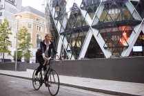 Businesswoman on bike passing 30 St Mary Axe, London, UK — Stock Photo
