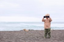 Toddler girl using binoculars on beach — Stock Photo