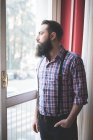Jeune homme barbu aux bretelles regardant par la porte — Photo de stock
