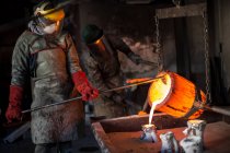 Trabajadores metalúrgicos trabajando en fundición, vertiendo bronce fundido - foto de stock