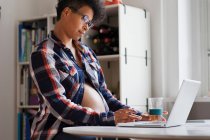 Pregnant woman using laptop in kitchen — Stock Photo