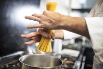 Chef putting spaghetti in saucepan on stove, close-up, overhead view — Stock Photo