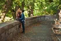 Молода пара обіймається на стіні в парку — стокове фото