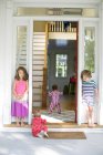 Garçon et fille regarder tout-petit ramper dans la porte de la maison — Photo de stock