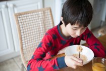 Мальчик ест хлопья на завтрак за столом — стоковое фото
